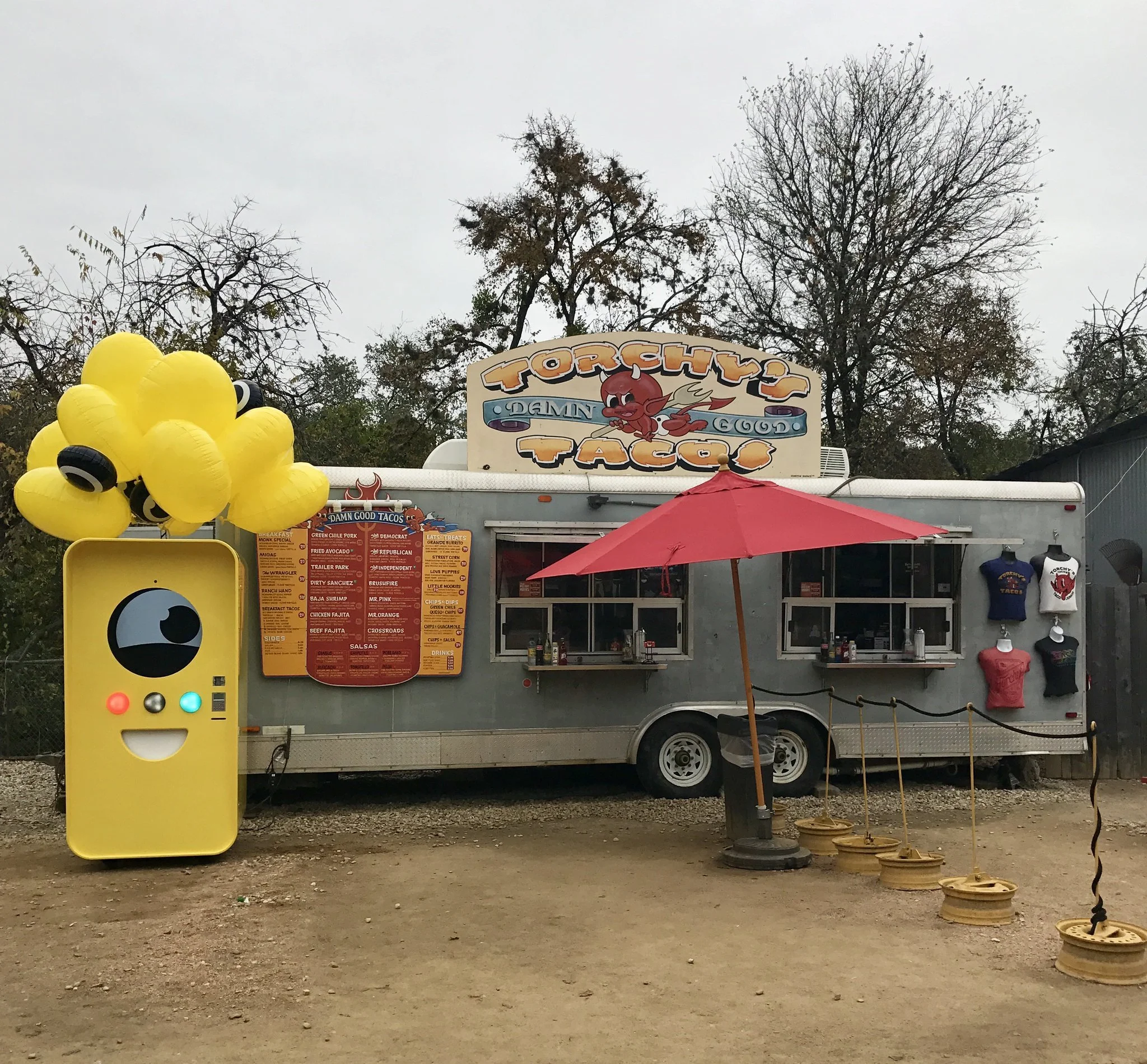 Yellow Snapbot vending machine with balloons parked on gravel beside the Torchy's Tacos silver airstream trailer